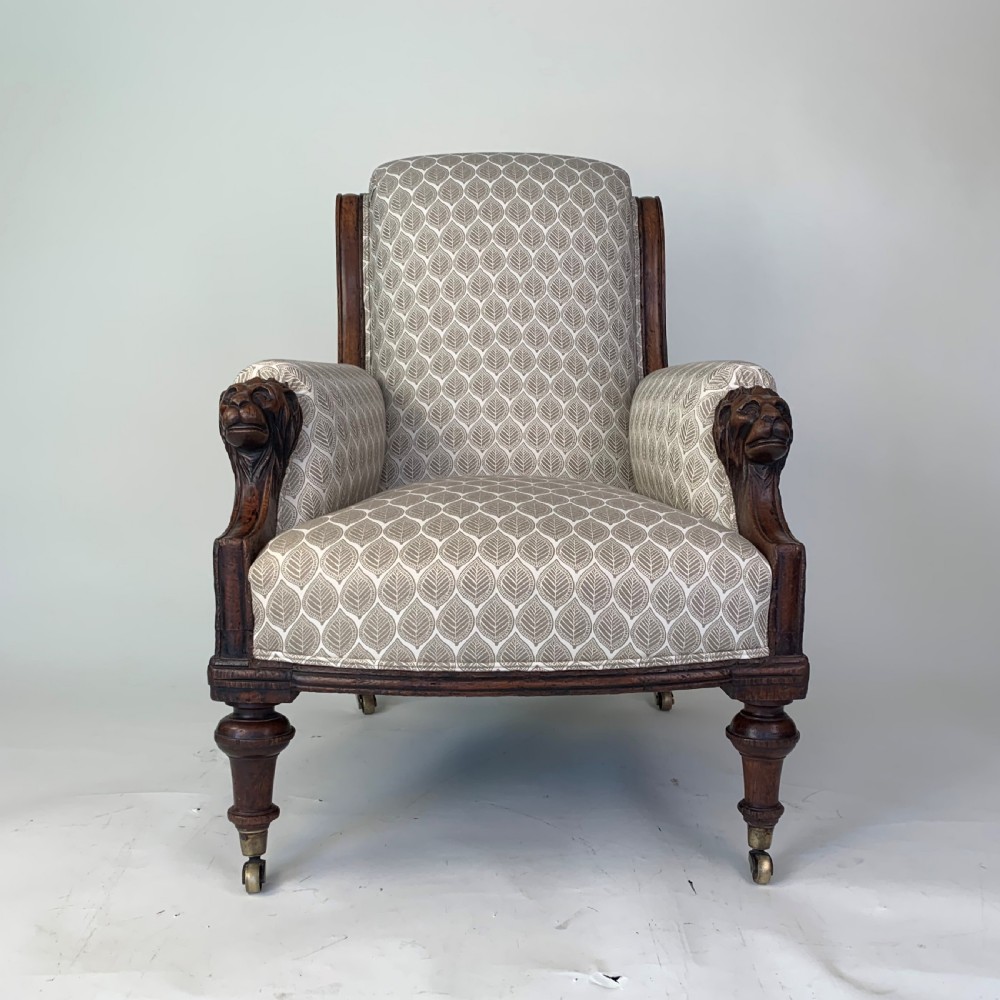 An antique high-back armchair featuring carved lion head armrests, turned wooden legs on castors, and patterned fabric upholstery. View III