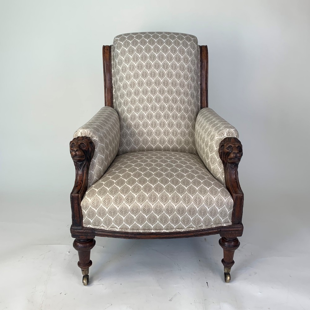 An antique high-back armchair featuring carved lion head armrests, turned wooden legs on castors, and patterned fabric upholstery. View V