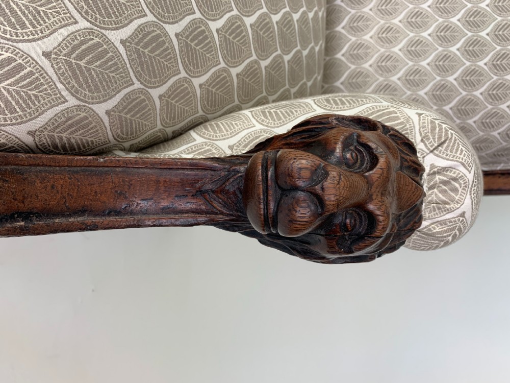 An antique high-back armchair featuring carved lion head armrests, turned wooden legs on castors, and patterned fabric upholstery. View XI