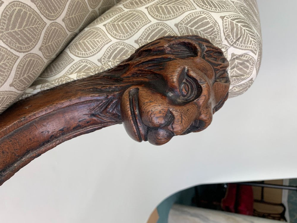 An antique high-back armchair featuring carved lion head armrests, turned wooden legs on castors, and patterned fabric upholstery. View XII