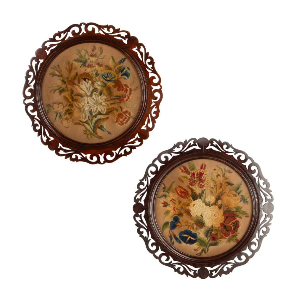 A pair of circular antique floral needlework panels housed within dark mahogany pierced openwork frames.