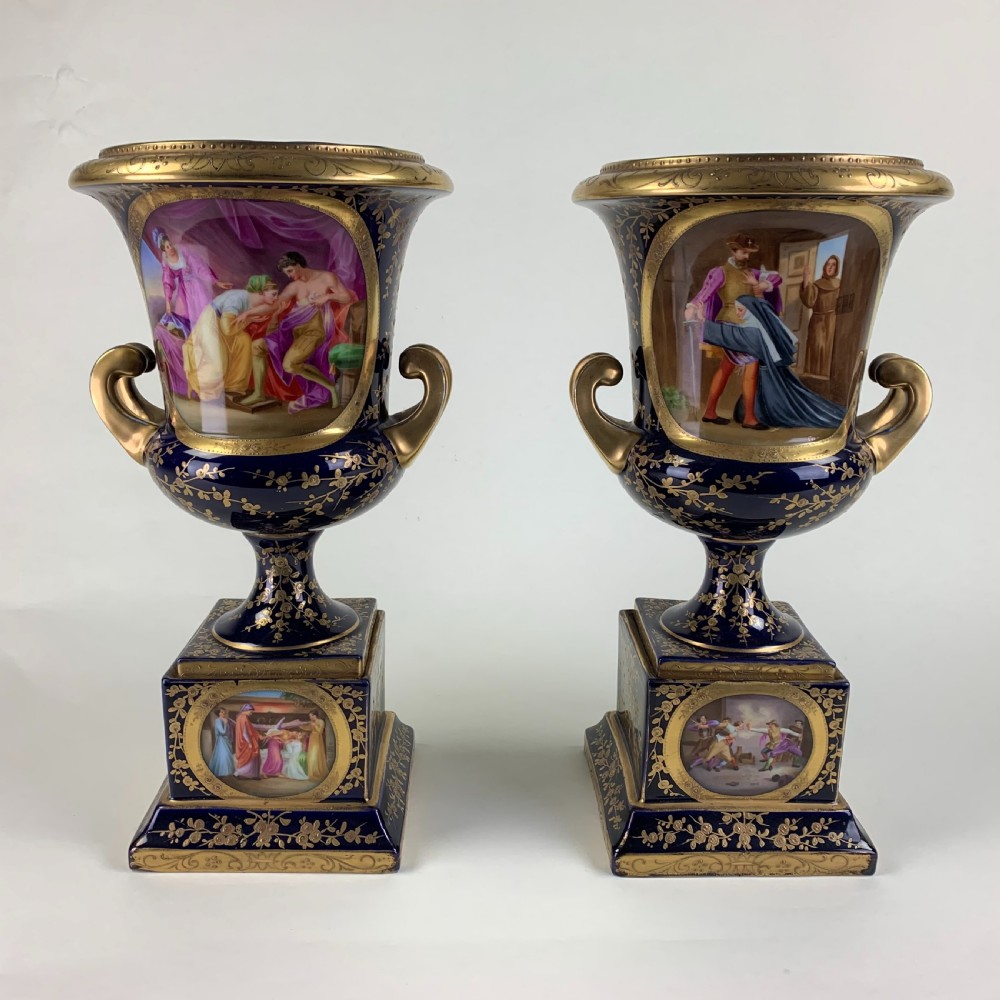 A pair of cobalt blue and gold Vienna porcelain urns with hand-painted classical scenes on square plinths.