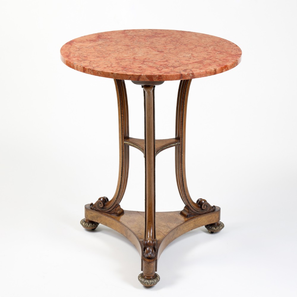 A circular occasional table featuring a reddish-pink marble top supported by a burr walnut frame with scrolled legs and a tripartite base.