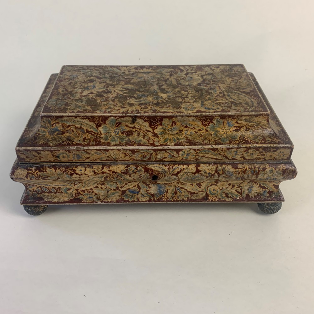 A rectangular early 19th-century Regency wooden games box, hand-painted with intricate botanical patterns in burgundy, gold, and green, featuring a sarcophagus-style lid and small ball feet. View II