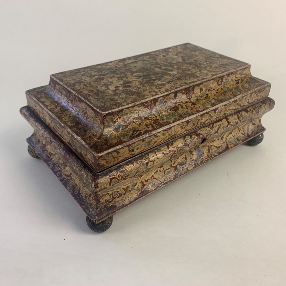 A rectangular early 19th-century Regency wooden games box, hand-painted with intricate botanical patterns in burgundy, gold, and green, featuring a sarcophagus-style lid and small ball feet. View III