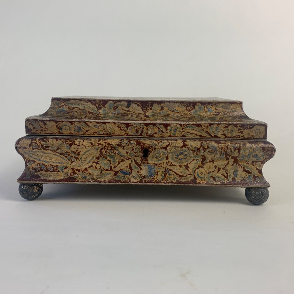 A rectangular early 19th-century Regency wooden games box, hand-painted with intricate botanical patterns in burgundy, gold, and green, featuring a sarcophagus-style lid and small ball feet. View V