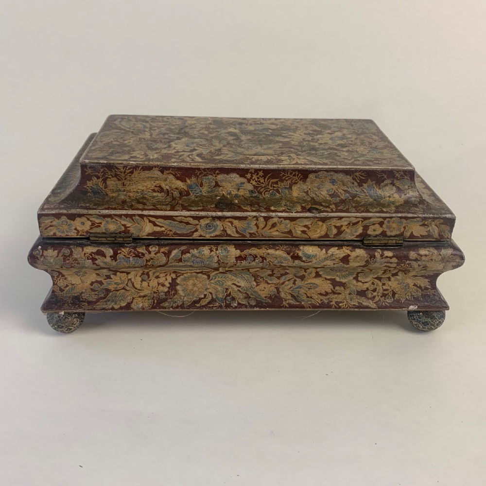 A rectangular early 19th-century Regency wooden games box, hand-painted with intricate botanical patterns in burgundy, gold, and green, featuring a sarcophagus-style lid and small ball feet. View VIII