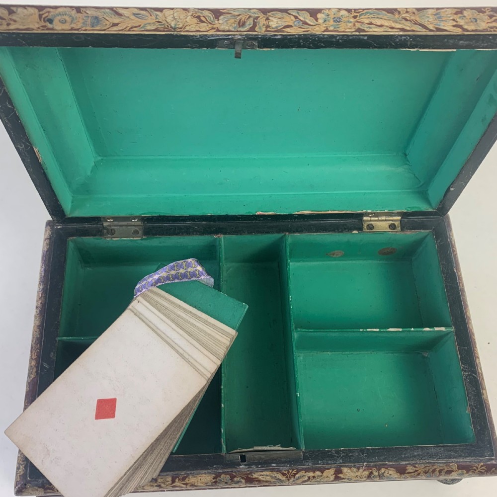 A rectangular early 19th-century Regency wooden games box, hand-painted with intricate botanical patterns in burgundy, gold, and green, featuring a sarcophagus-style lid and small ball feet. View X
