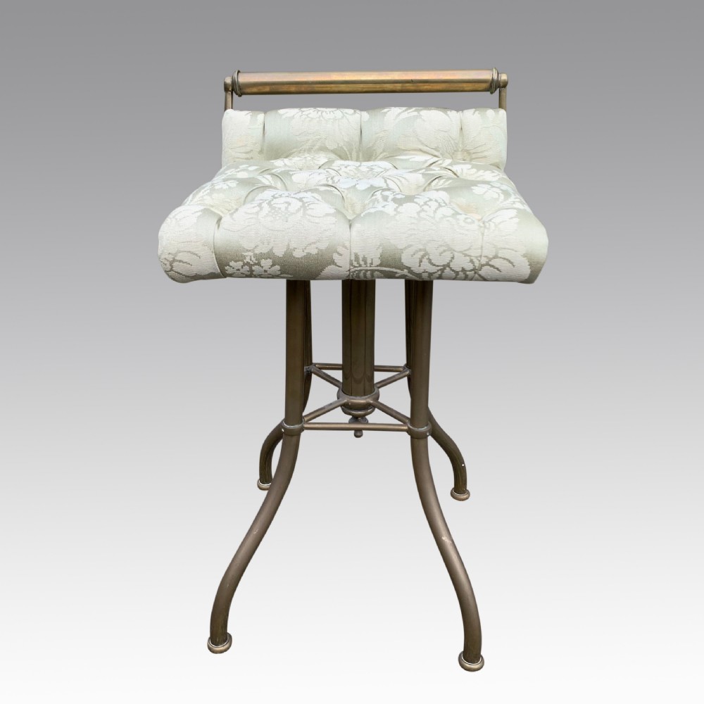 An upright brass pianochello music stool featuring an upholstered cream patterned seat and a curved back rail. View II