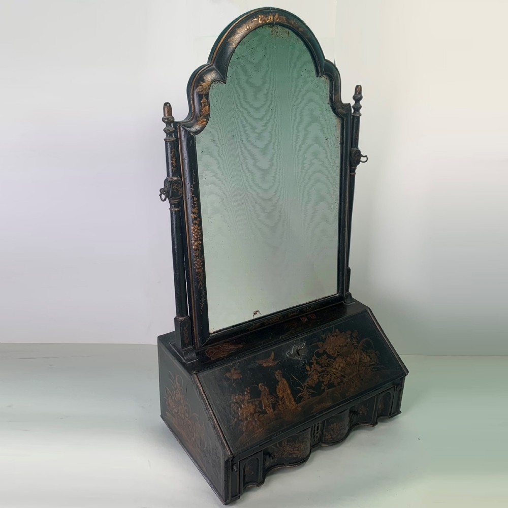 A black lacquered toilet mirror featuring an arched frame and gilded Chinoiserie artwork mounted on a miniature slant-front bureau base.