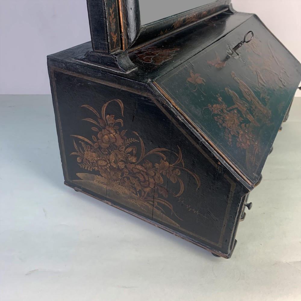 A black lacquered toilet mirror featuring an arched frame and gilded Chinoiserie artwork mounted on a miniature slant-front bureau base. View V