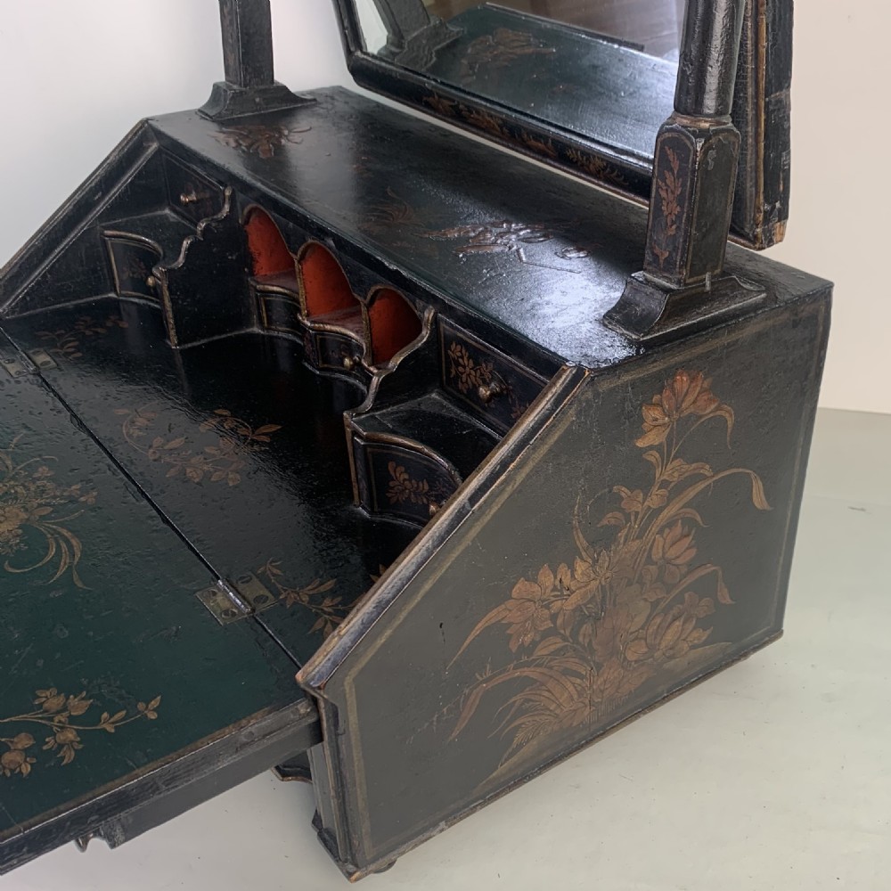 A black lacquered toilet mirror featuring an arched frame and gilded Chinoiserie artwork mounted on a miniature slant-front bureau base. View X