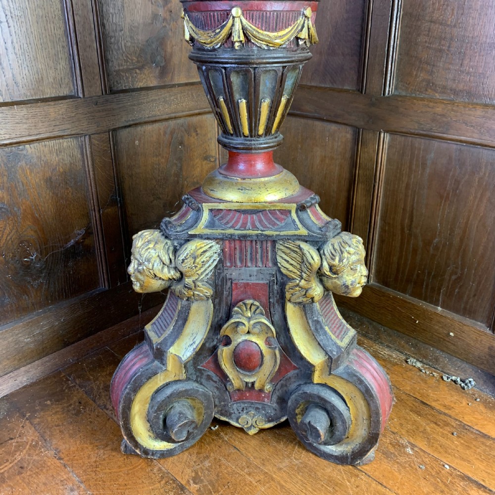 A tall, ornately carved Italian wooden torchiere featuring red and gold polychrome finishes, turned central column sections, and a sculptural scroll base. View V