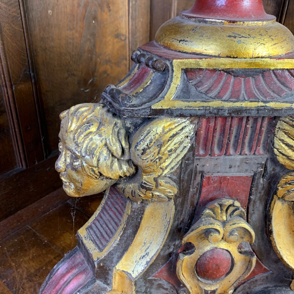 A tall, ornately carved Italian wooden torchiere featuring red and gold polychrome finishes, turned central column sections, and a sculptural scroll base. View VI