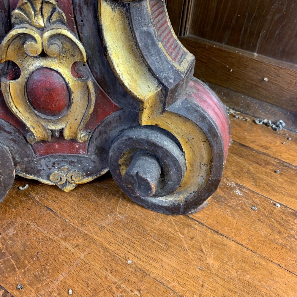 A tall, ornately carved Italian wooden torchiere featuring red and gold polychrome finishes, turned central column sections, and a sculptural scroll base. View VII