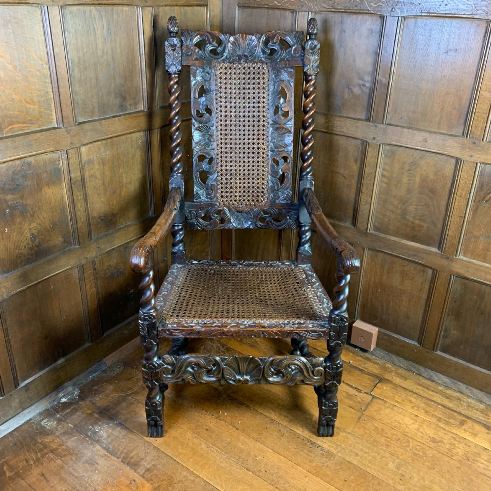 A 17th-century Carolean dark walnut armchair featuring a high backrest with woven cane panels, intricate spiral turned legs, and detailed foliage carving.