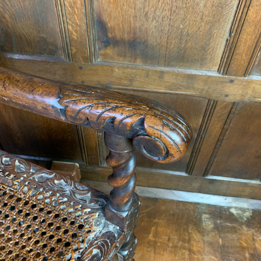 A 17th-century Carolean dark walnut armchair featuring a high backrest with woven cane panels, intricate spiral turned legs, and detailed foliage carving. View V