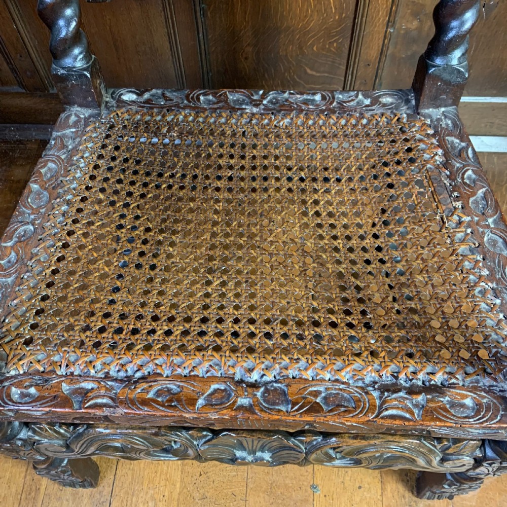 A 17th-century Carolean dark walnut armchair featuring a high backrest with woven cane panels, intricate spiral turned legs, and detailed foliage carving. View VI
