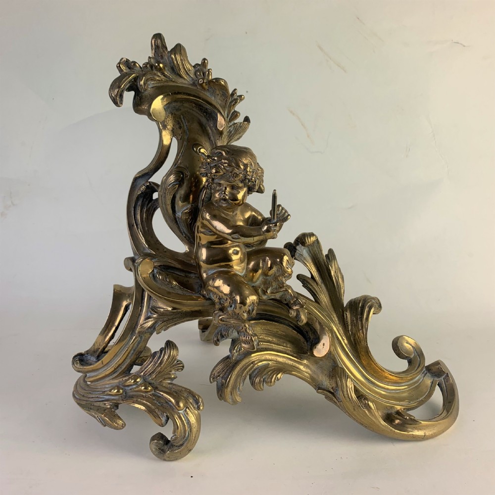 A pair of ornate gilded brass chenets featuring sculpted cherub figures seated amidst asymmetrical leaf scrolls and rocaille motifs. View III