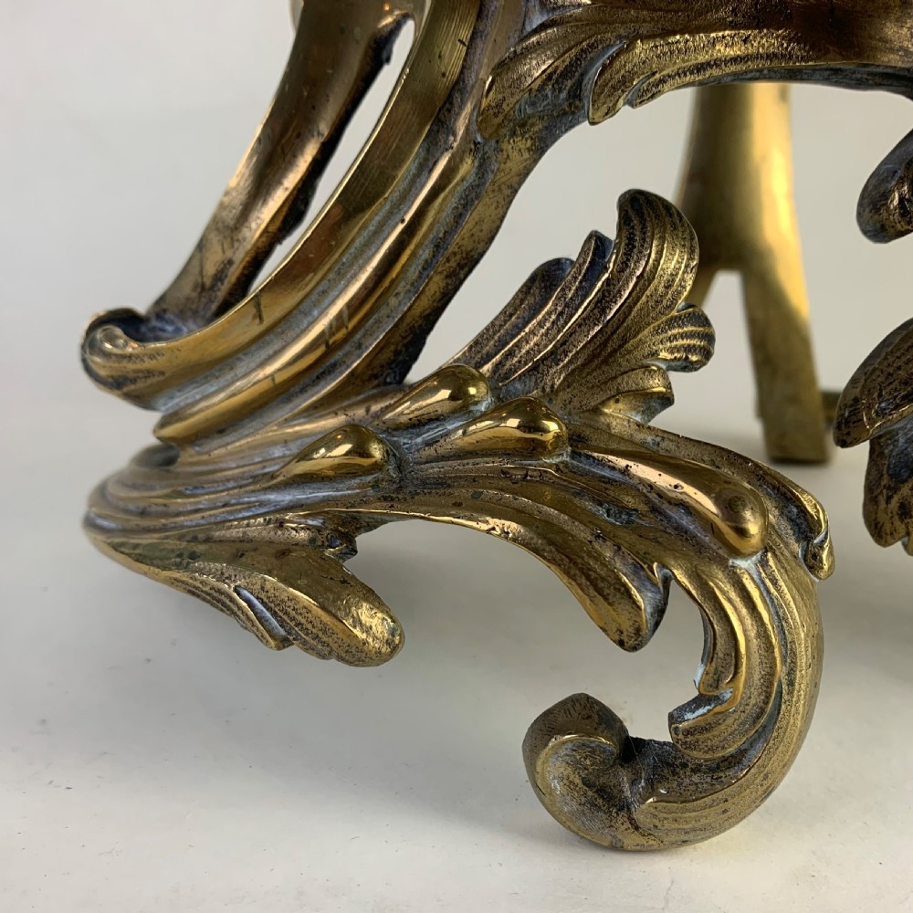 A pair of ornate gilded brass chenets featuring sculpted cherub figures seated amidst asymmetrical leaf scrolls and rocaille motifs. View VI