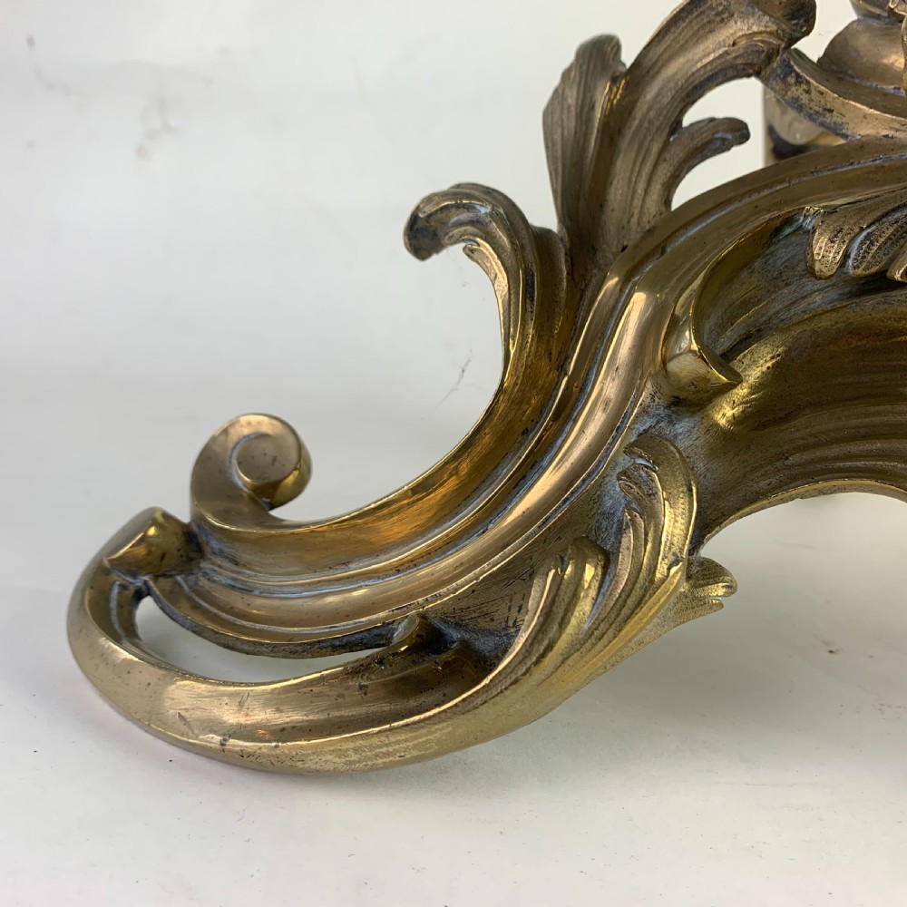 A pair of ornate gilded brass chenets featuring sculpted cherub figures seated amidst asymmetrical leaf scrolls and rocaille motifs. View VIII