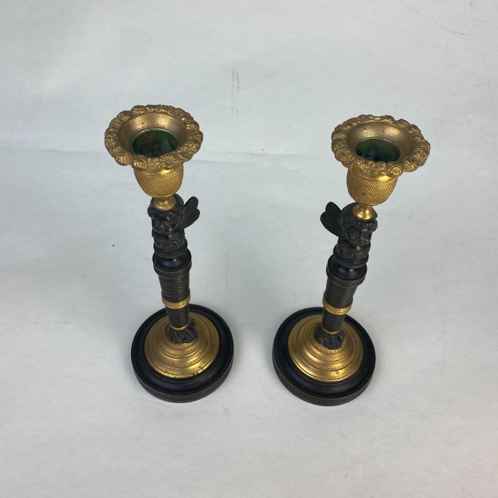 A pair of antique patinated bronze and ormolu candlesticks featuring central putti busts supporting urn sconces set on circular gilded bases. View III