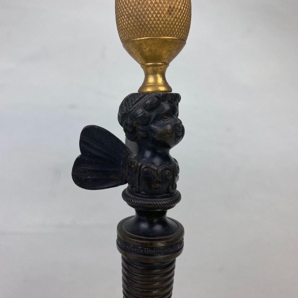 A pair of antique patinated bronze and ormolu candlesticks featuring central putti busts supporting urn sconces set on circular gilded bases. View IV