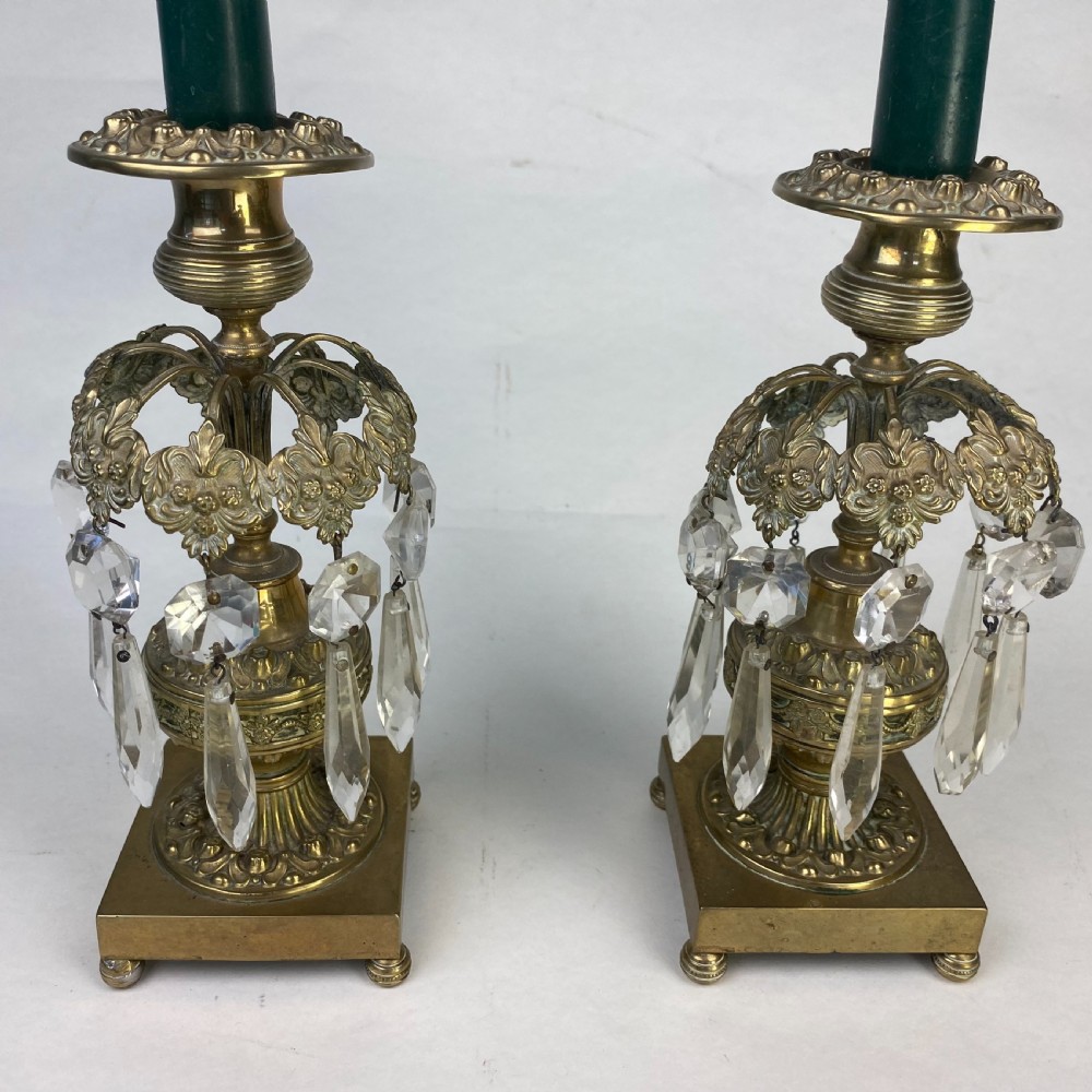 A pair of ornate gilt metal candlesticks featuring square plinth bases, decorative scrollwork rims, and clear cut glass lustre drops hanging around the column. View II