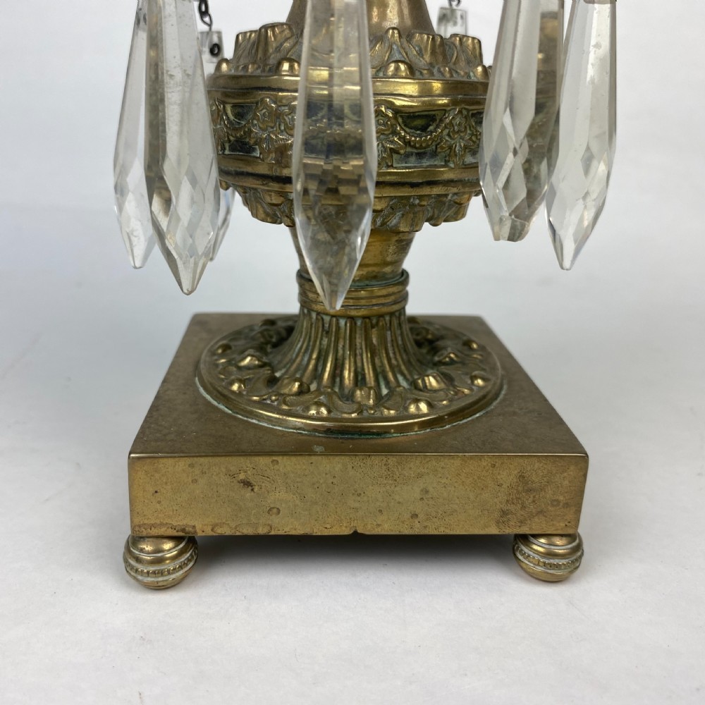 A pair of ornate gilt metal candlesticks featuring square plinth bases, decorative scrollwork rims, and clear cut glass lustre drops hanging around the column. View IV
