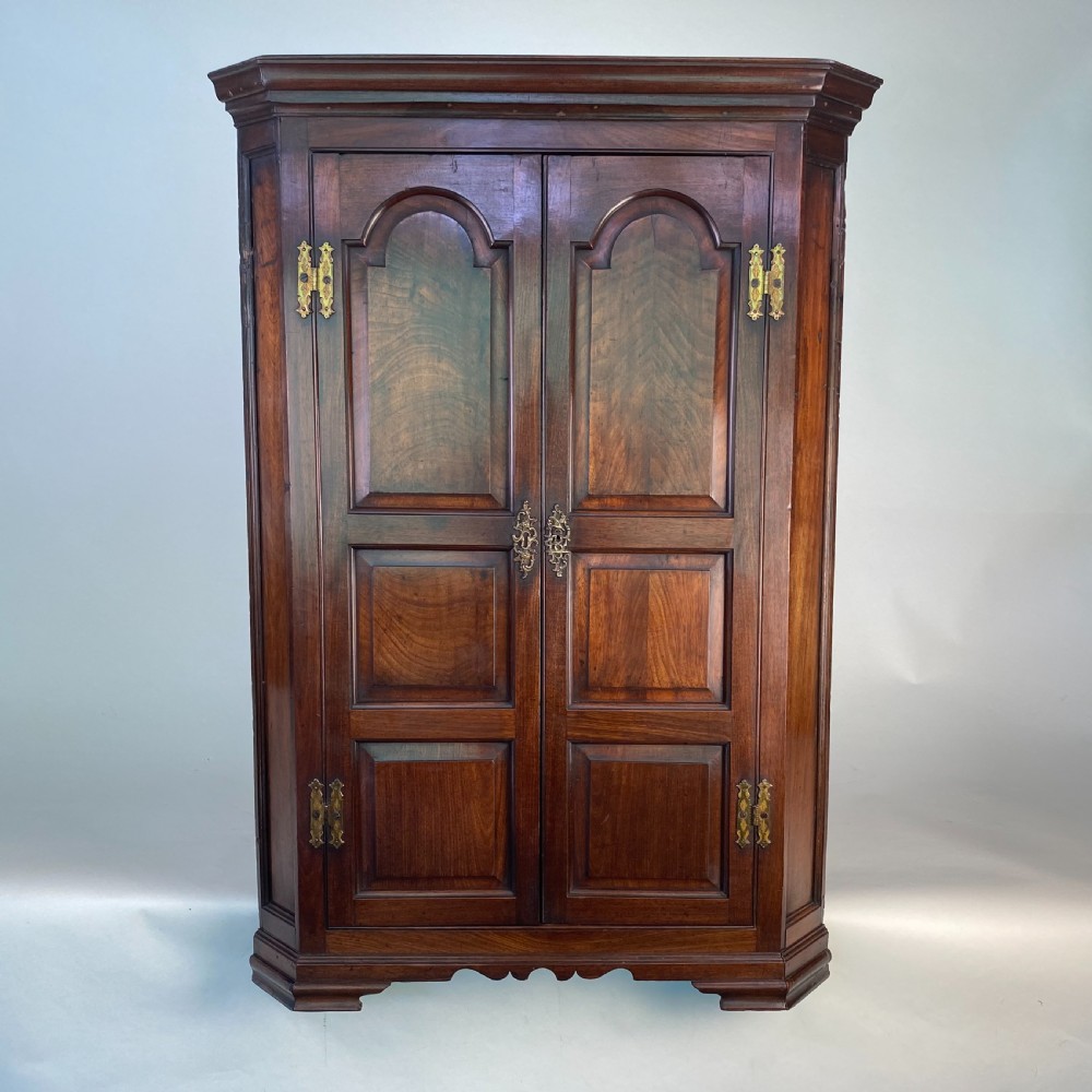 An antique Georgian mahogany corner cupboard with twin panelled doors, arched top panels, and brass hinges.