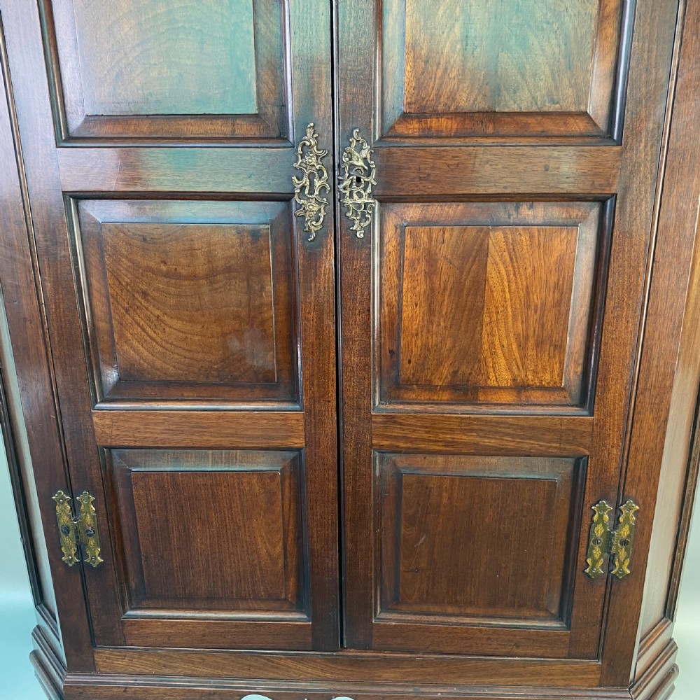 An antique Georgian mahogany corner cupboard with twin panelled doors, arched top panels, and brass hinges. View V