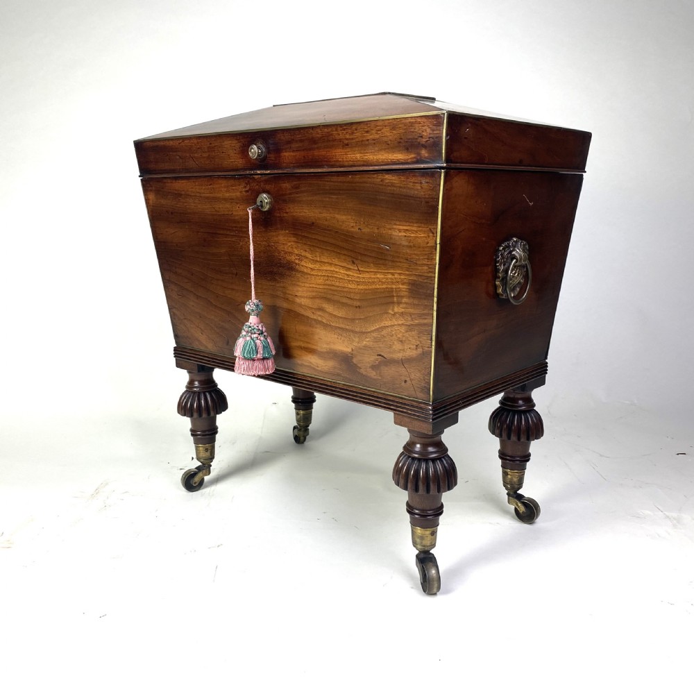 A Regency mahogany sarcophagus-shaped cellarette featuring brass inlay, side lion mask handles, and fluted legs with castors. View II
