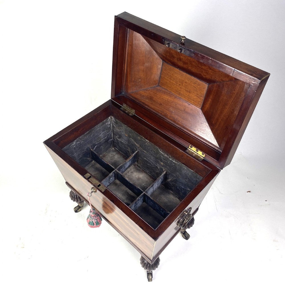 A Regency mahogany sarcophagus-shaped cellarette featuring brass inlay, side lion mask handles, and fluted legs with castors. View IV