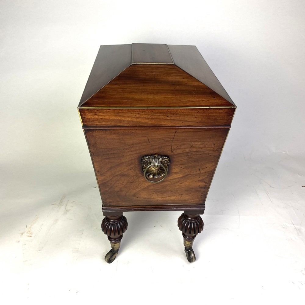 A Regency mahogany sarcophagus-shaped cellarette featuring brass inlay, side lion mask handles, and fluted legs with castors. View VI