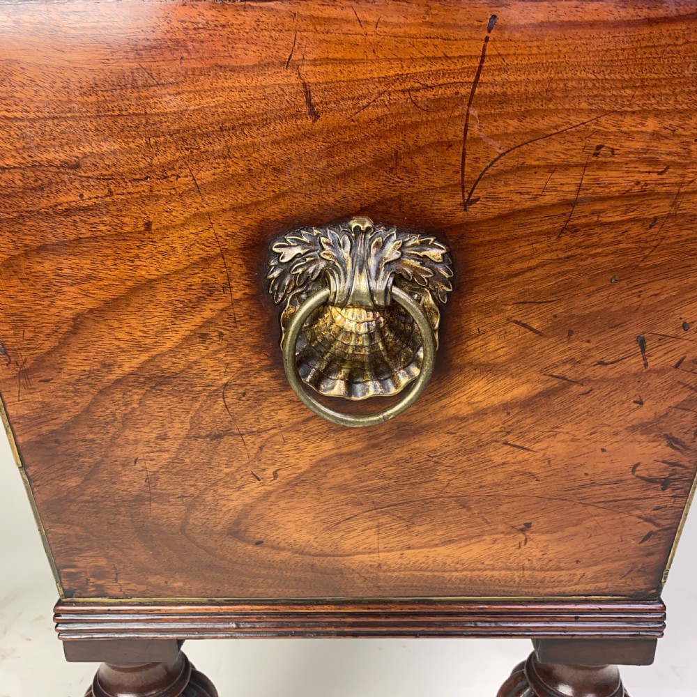 A Regency mahogany sarcophagus-shaped cellarette featuring brass inlay, side lion mask handles, and fluted legs with castors. View VII