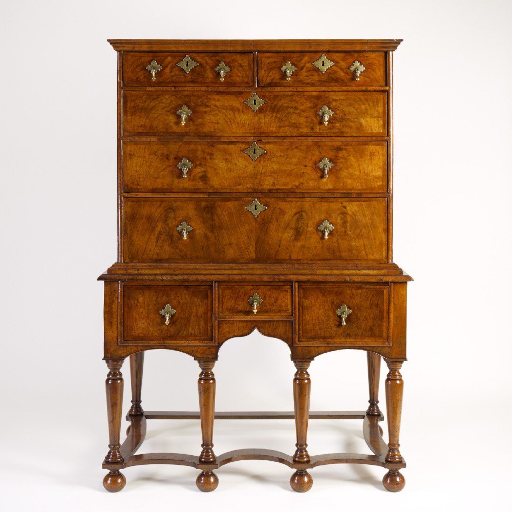 A Queen Anne walnut chest on stand featuring multiple drawers with brass hardware, six turned legs, and a shaped wavy stretcher base.