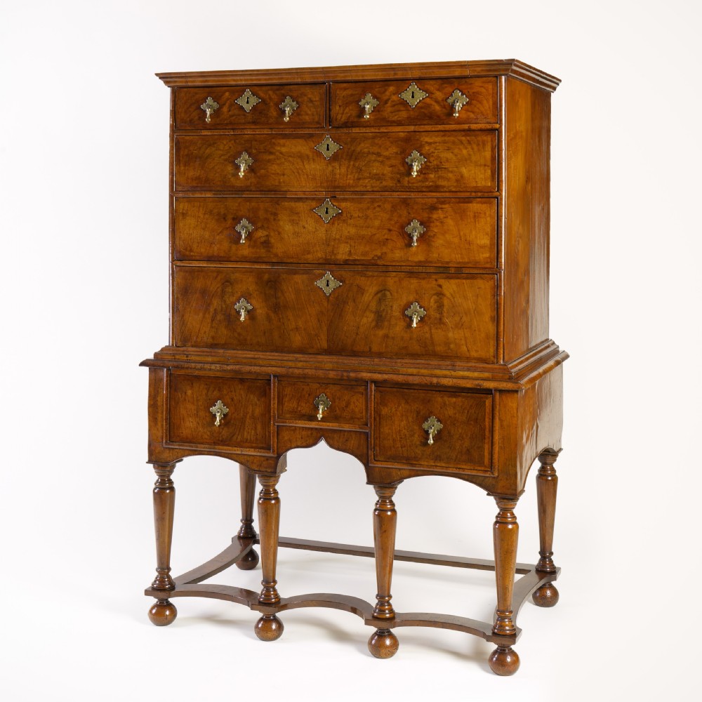 A Queen Anne walnut chest on stand featuring multiple drawers with brass hardware, six turned legs, and a shaped wavy stretcher base. View II