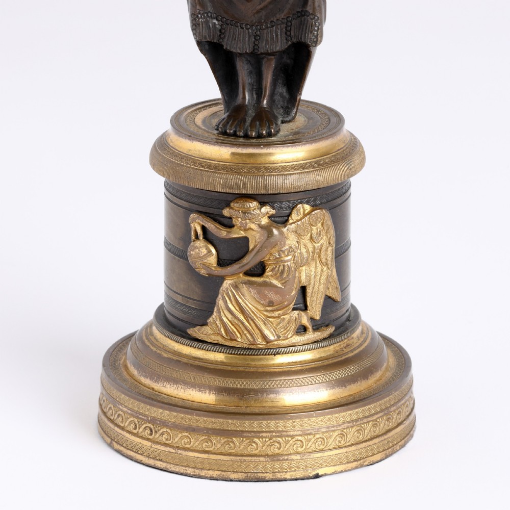 A pair of antique dark bronze figural candlesticks depicting classical draped female figures standing on ornate round gilt bronze bases holding acanthus leaf sconces. View III