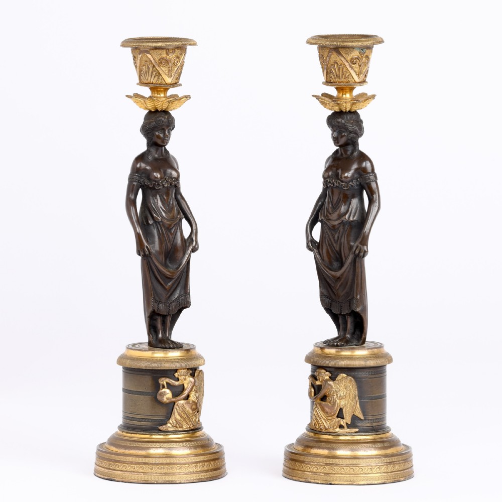A pair of antique dark bronze figural candlesticks depicting classical draped female figures standing on ornate round gilt bronze bases holding acanthus leaf sconces. View IV
