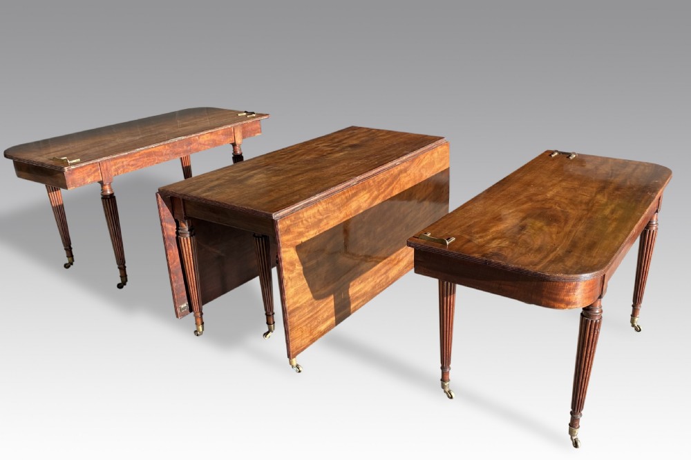 An extended mahogany dining table displaying multiple leaf sections, reeded tapered legs, and brass castors. View VII