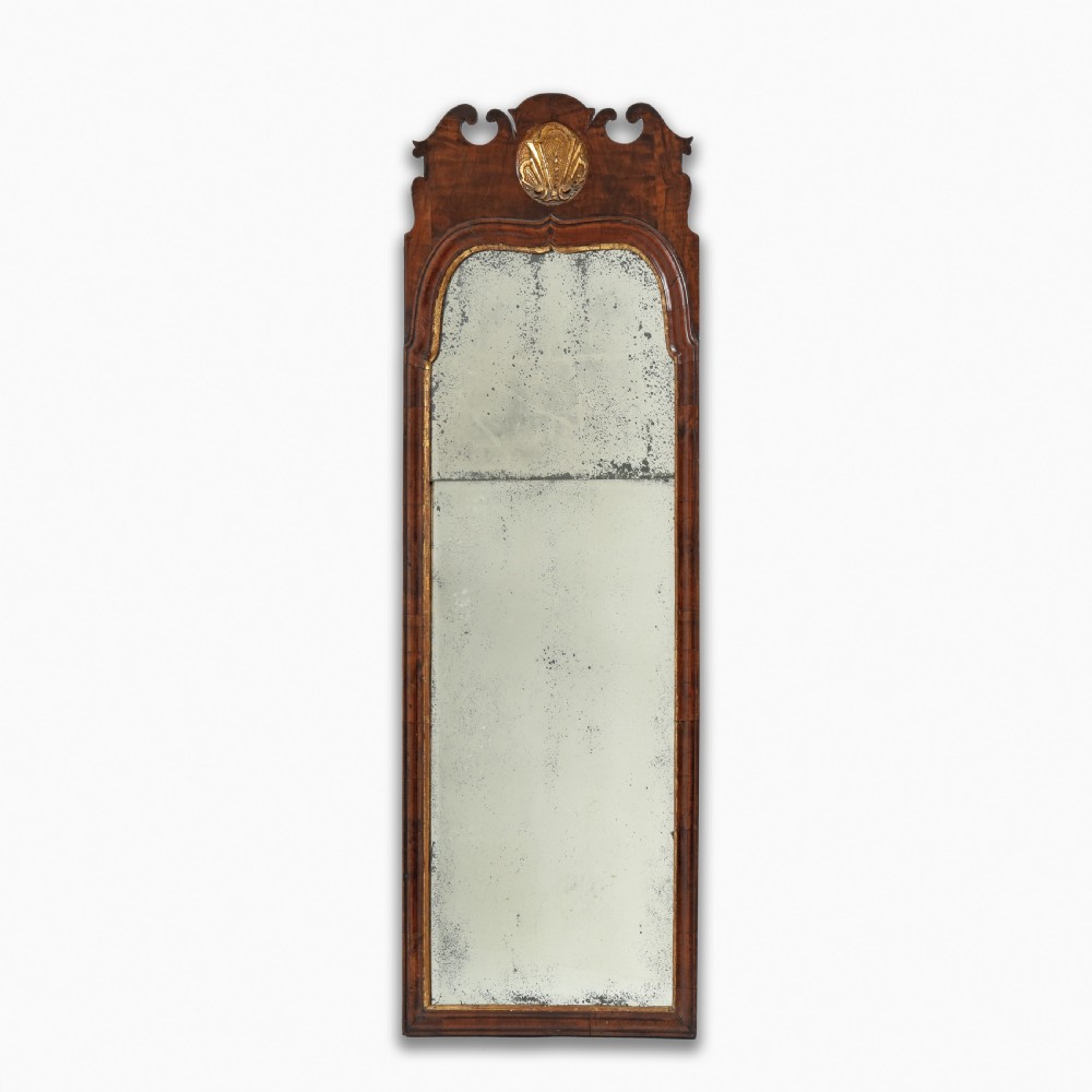 A tall Queen Anne walnut pier mirror featuring an arched frame with a carved gilded shell crest and two-section foxed mirror glass.