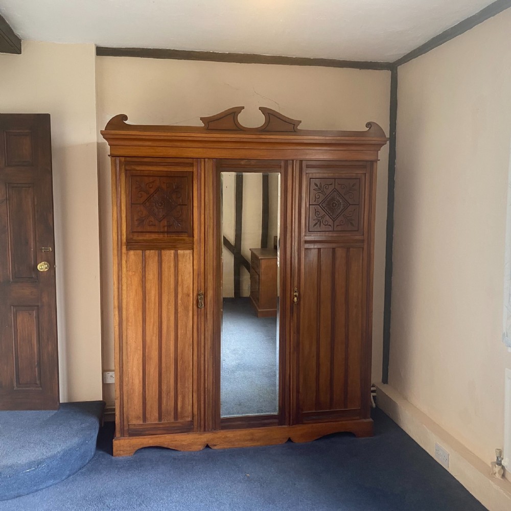 A nineteenth-century Victorian walnut triple wardrobe featuring a central full-length mirrored door flanked by two carved wooden panel doors and topped with a decorative pediment.