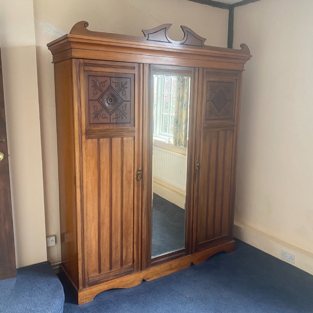 A nineteenth-century Victorian walnut triple wardrobe featuring a central full-length mirrored door flanked by two carved wooden panel doors and topped with a decorative pediment. View II