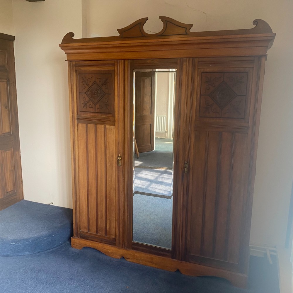 A nineteenth-century Victorian walnut triple wardrobe featuring a central full-length mirrored door flanked by two carved wooden panel doors and topped with a decorative pediment. View III