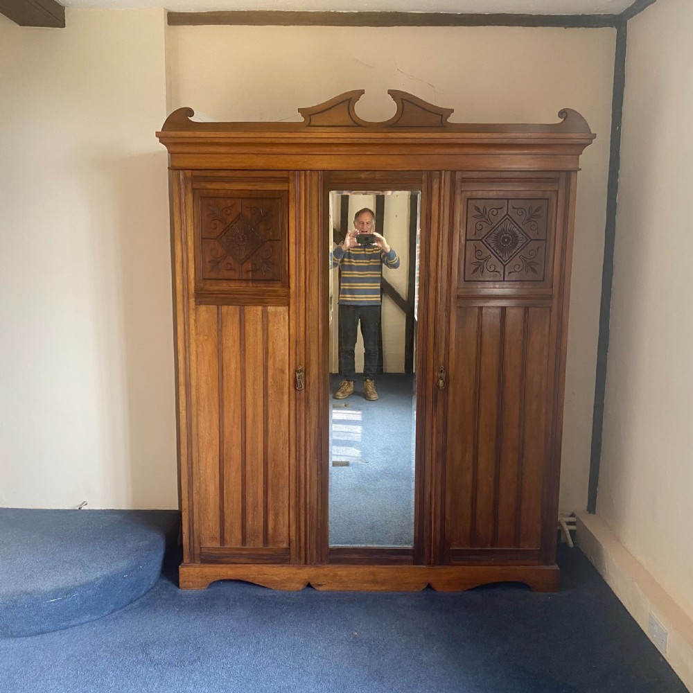 A nineteenth-century Victorian walnut triple wardrobe featuring a central full-length mirrored door flanked by two carved wooden panel doors and topped with a decorative pediment. View V