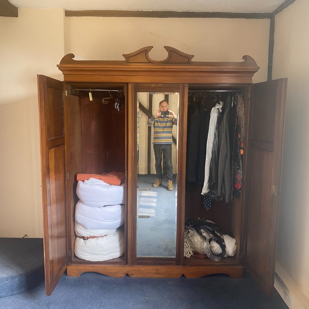 A nineteenth-century Victorian walnut triple wardrobe featuring a central full-length mirrored door flanked by two carved wooden panel doors and topped with a decorative pediment. View VI
