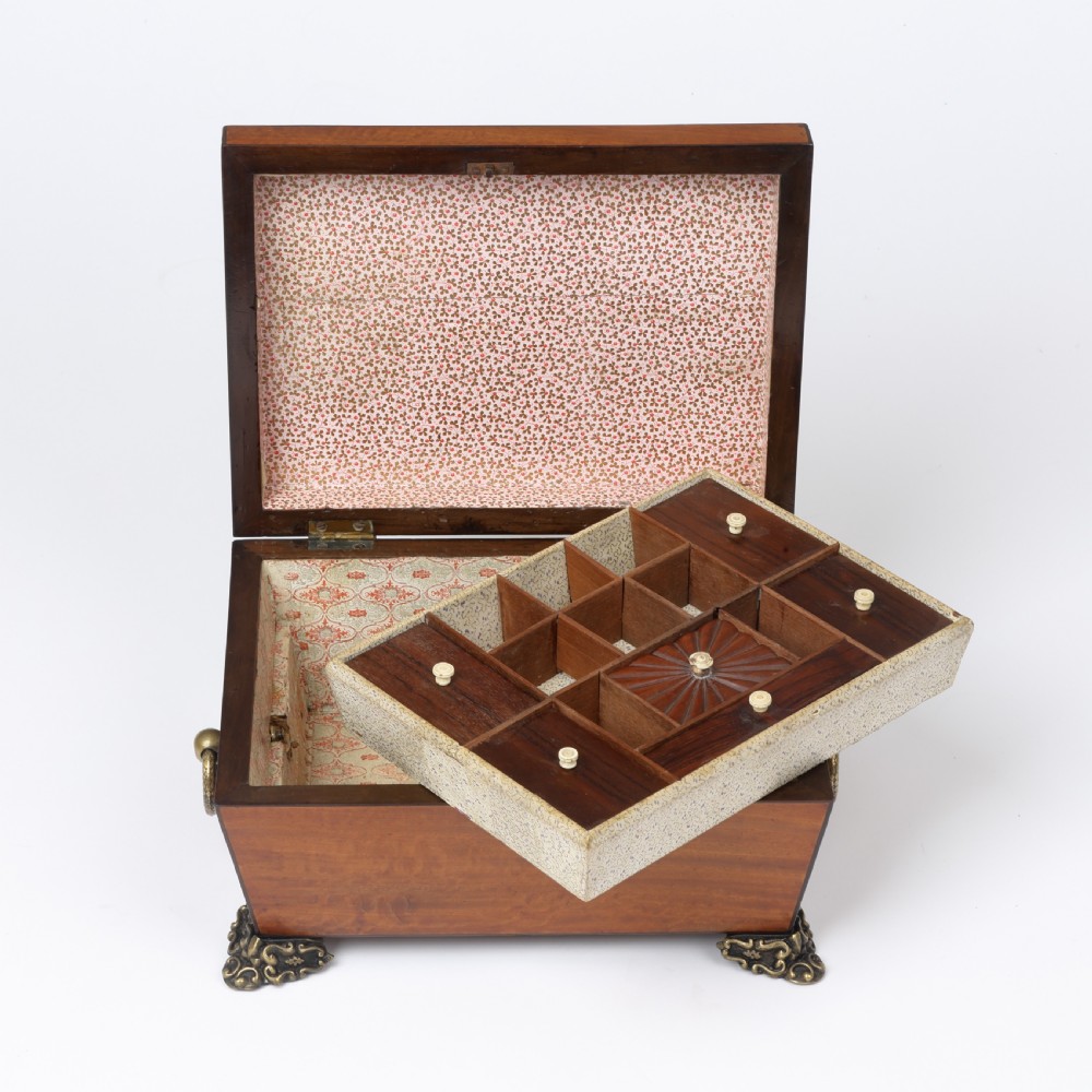 A Regency style satinwood casket box featuring a tapered sarcophagus shape, carved lid trim, brass claw feet, and side ring handles. View II
