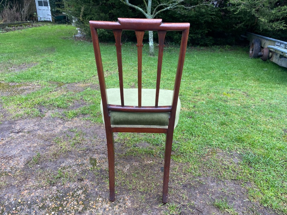 A set of seven mahogany dining chairs, including six side chairs and one carver armchair, with square backs and green velvet seats. View X