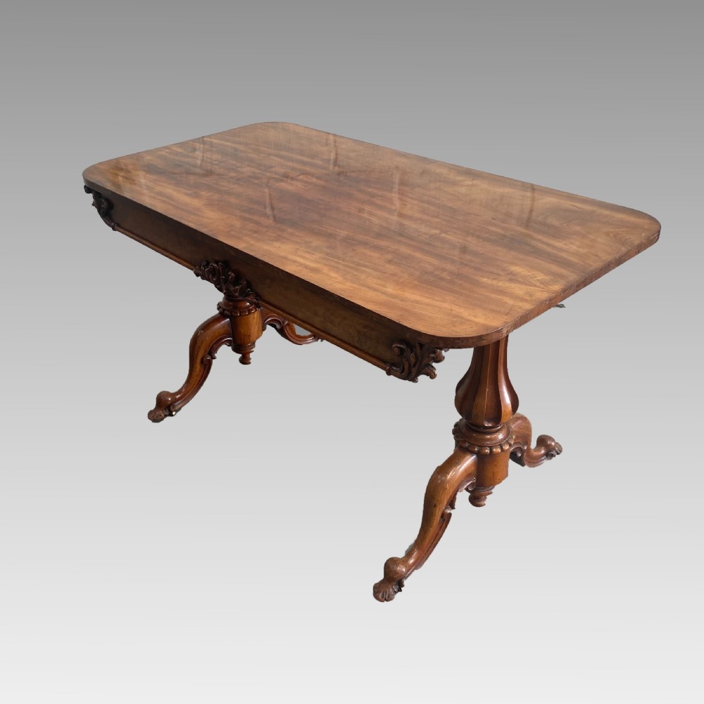 An early 19th-century mahogany library table with a polished rectangular top, carved aprons, and turned pedestal supports resting on scrolled feet.