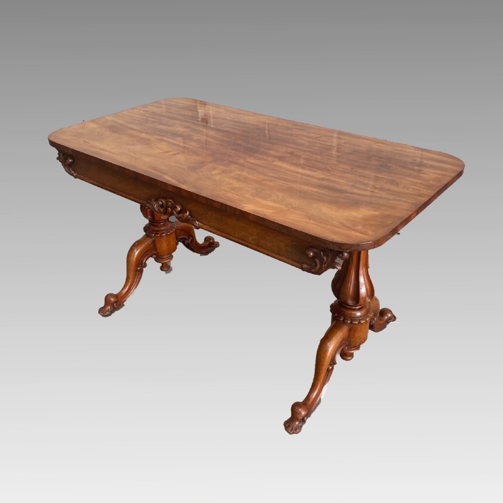 An early 19th-century mahogany library table with a polished rectangular top, carved aprons, and turned pedestal supports resting on scrolled feet. View II